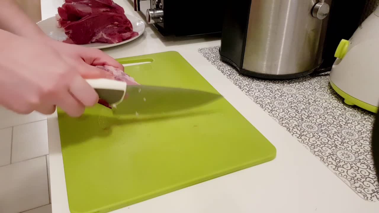 Mulher caucasiana cortando carne de porco com uma faca branca em uma tábua verde