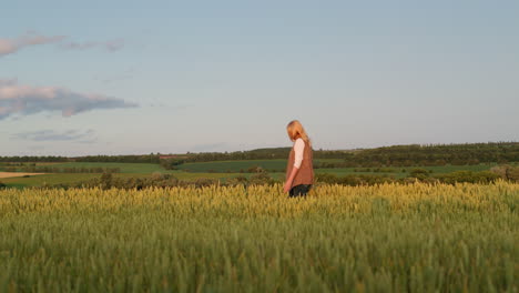 Eine-Frau-Geht-Durch-Ein-Weizenfeld-Vor-Der-Kulisse-Einer-Malerischen-Ländlichen-Landschaft.-Seitenansicht