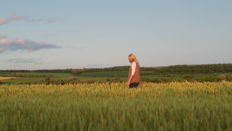 a woman walks through a field of wheat against the backdrop of a picturesque rural landscape. side view