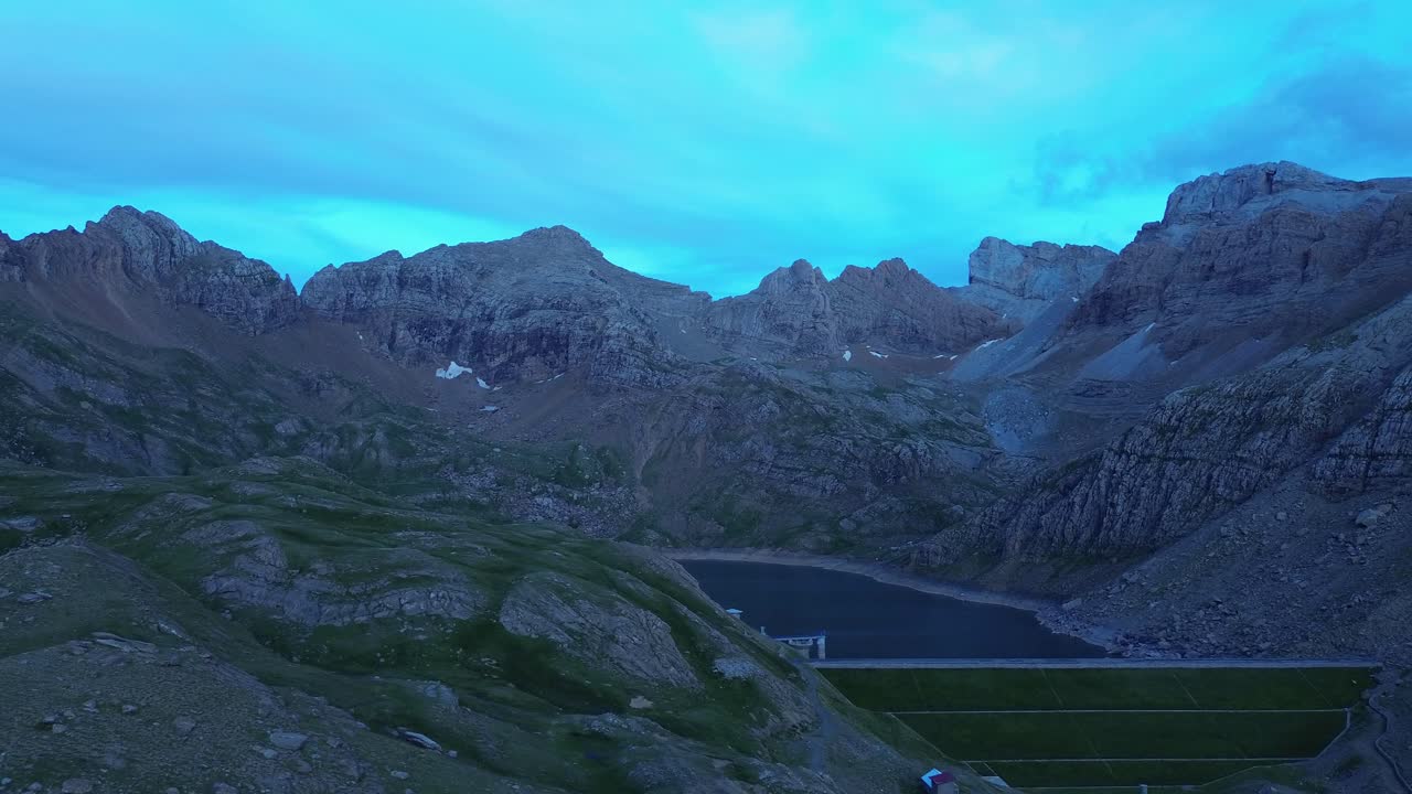 Sweeping aerial footage captures Valle de Ip near Canfranc, Aragón, Spain. Rugged mountains bathed in serene blue dusk light create a breathtaking and tranquil atmosphere