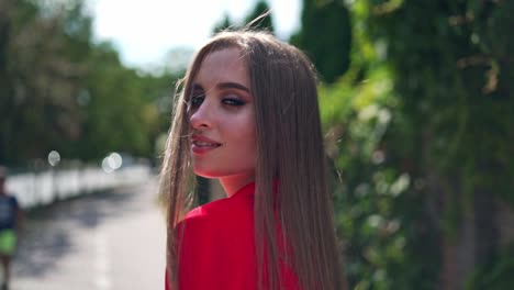 attractive girl outdoors in summer. long-haired woman in passionate red dress looking on camera and smiling in the city street. slow motion.
