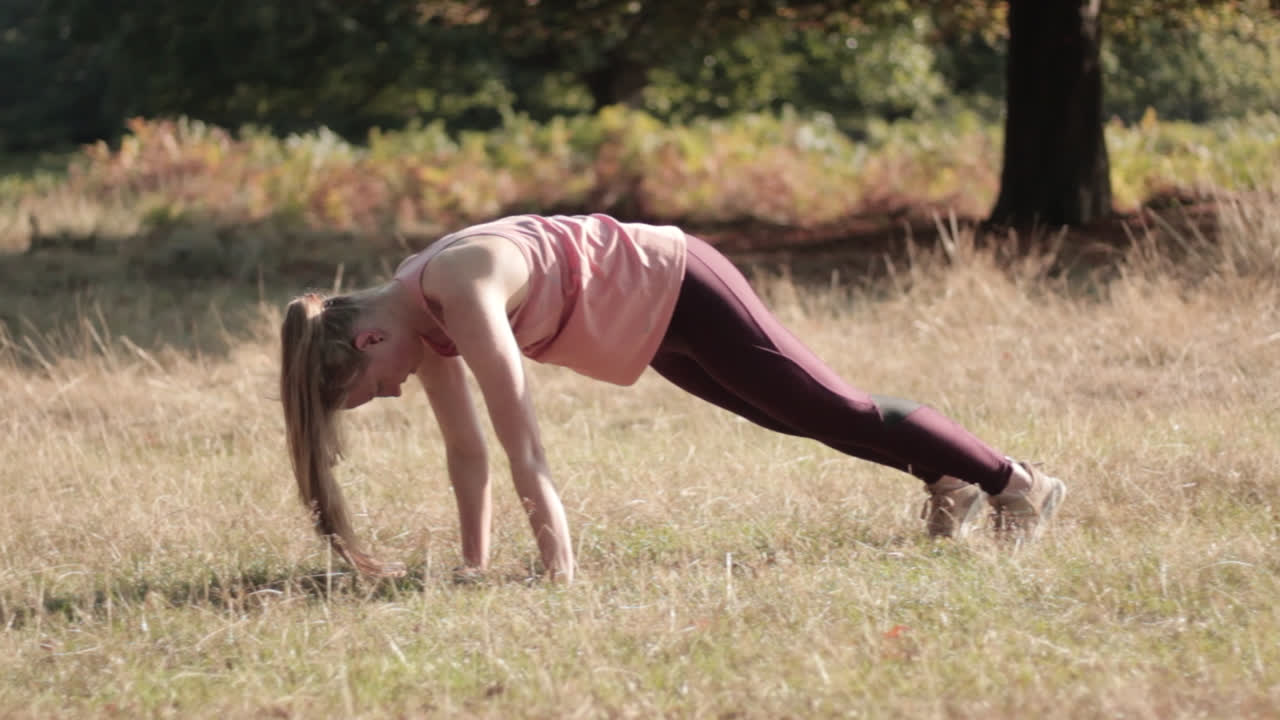 en el parque en un día soleado, una mujer joven está ejerciendo sus poses de yoga mientras está de pie en las posiciones de perro boca abajo y adho mukha savasana