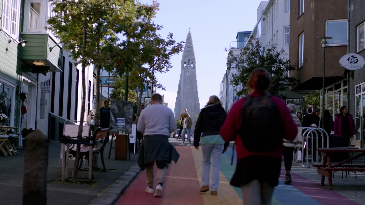 People walking on a colorful street towards Hallgrímskirkja in Reykjavik on a clear day