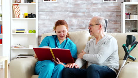 social worker reading to an old and disabled man sitting on a sofa in nursing home