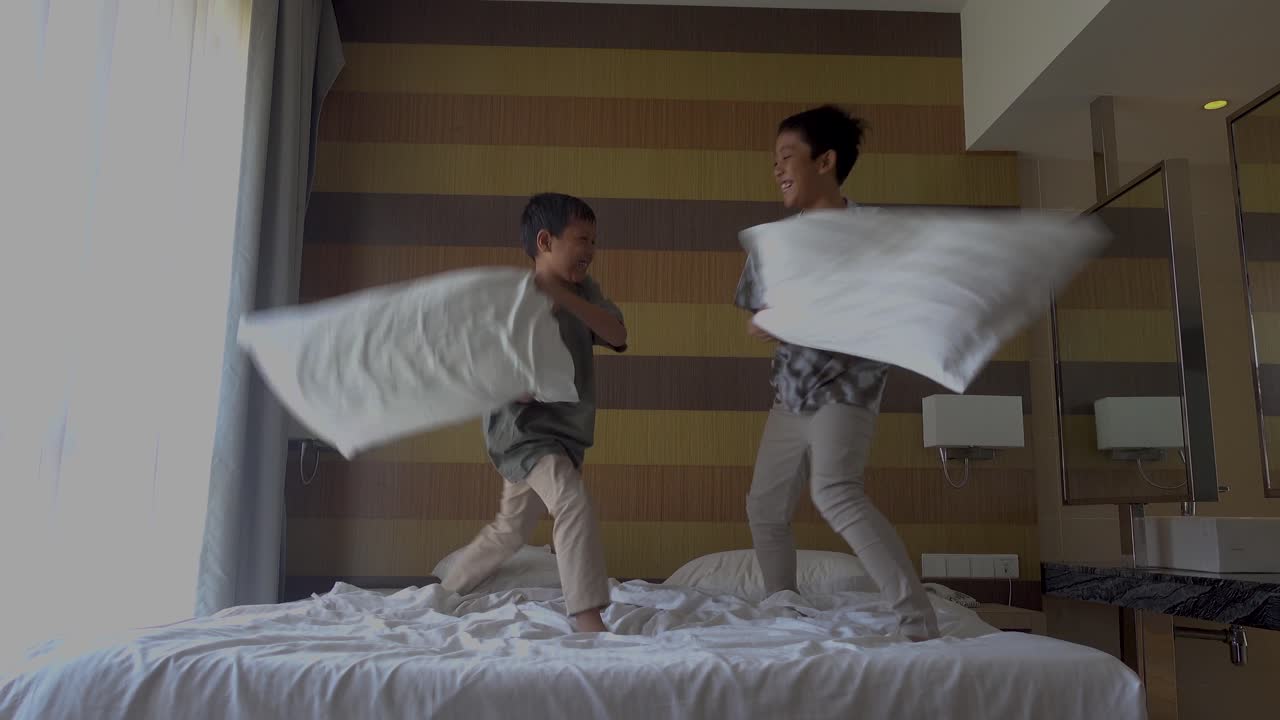 Two brothers doing pillow fight on bed in the morning, laughing having fun together. Leisure time, happy family and joyful people concept.