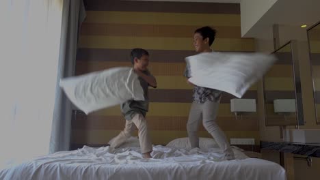 two brothers doing pillow fight on bed in the morning, laughing having fun together. leisure time, happy family and joyful people concept.