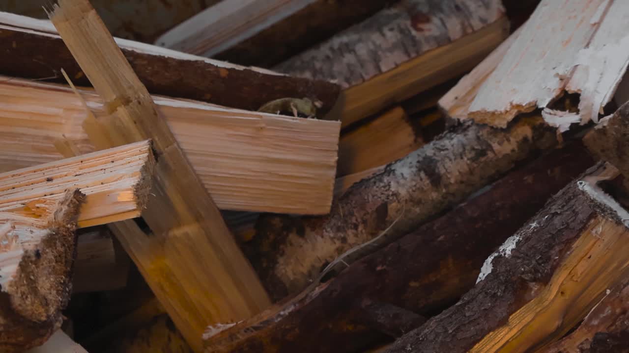 Close up view panning over freshly broken and split pine and birch firewood logs or timber on top of each other in a pile during sunny autumn or summer day at a home garden. Shallow depth of field