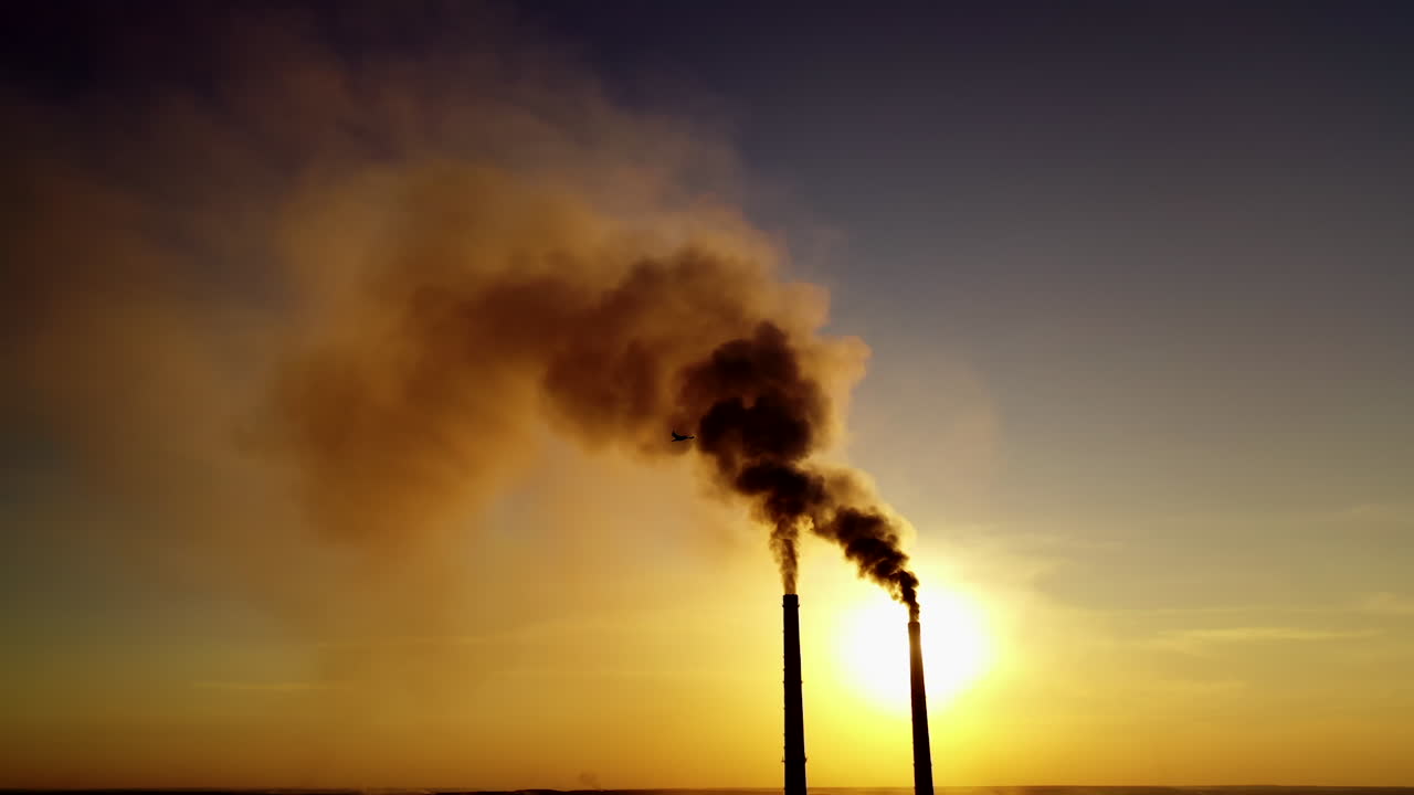 Two industrial pipes with dark smoke at sunset. Massive dense of toxic emissions from industrial factory filling the sky in the evening. Polluting the atmosphere.