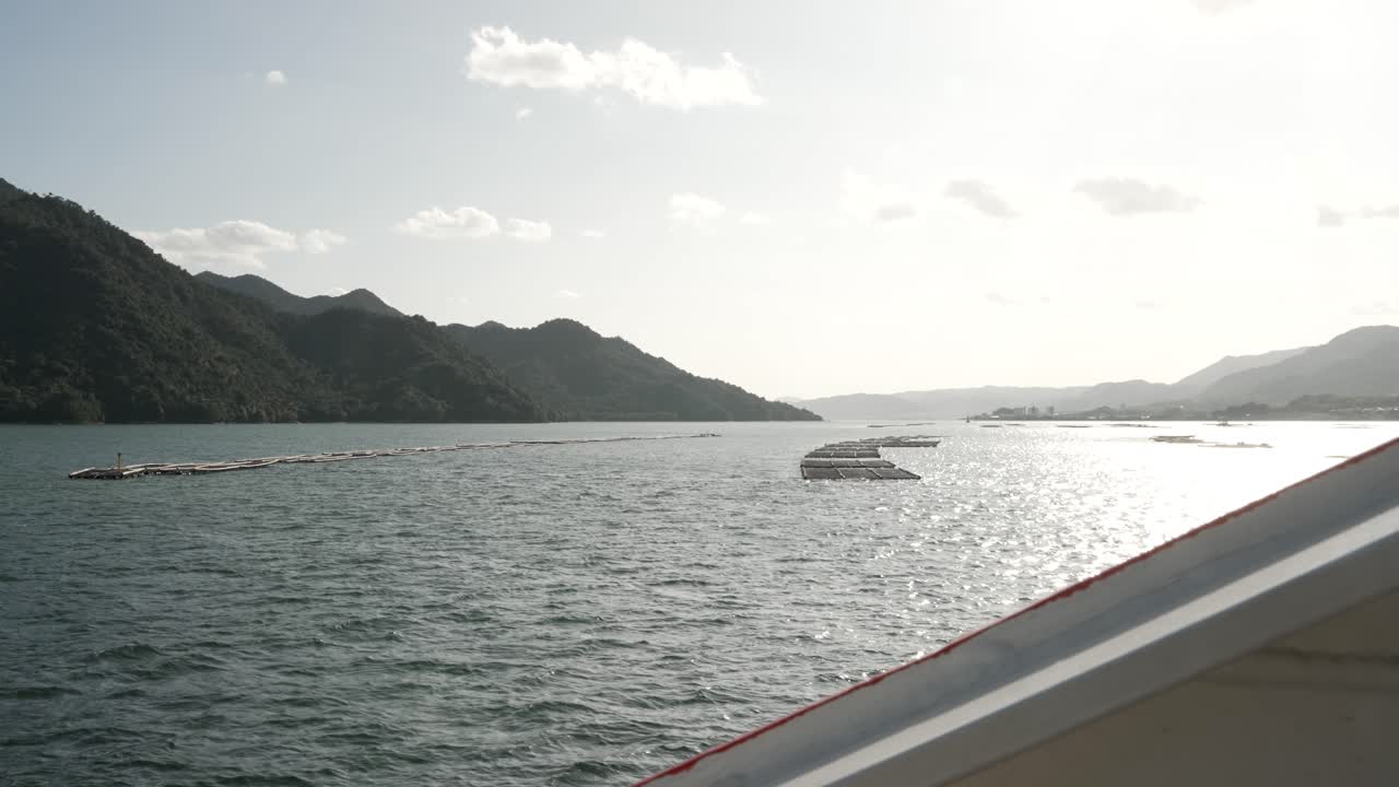 Vorbeifahrt an Reihen schwimmender Austernfarmen in der Bucht von Hiroshima, goldenes Sonnenlicht auf der Wasseroberfläche