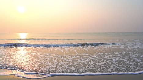 Eine-Goldene-Sonne-Versinkt-Im-Meereshorizont,-Während-Die-Brandung-Auf-Den-Strand-Trifft