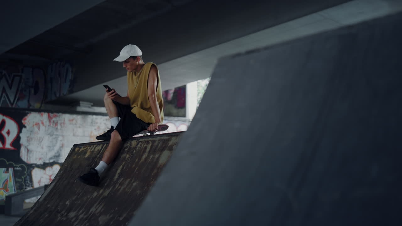 Stylish man browsing internet online on mobile phone at skatepark with graffiti.