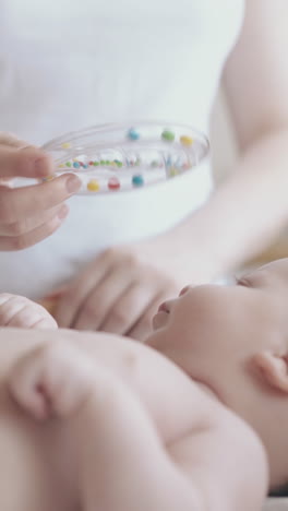 cute infant lies on changing table mother distracts attention holding plastic toy and nurse massages legs close view
