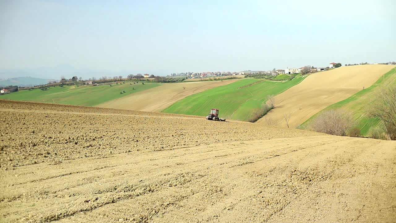 경작지 농장이 있는 이탈리아 시골에서 오르막길을 운전하는 트랙터, 계절 농업 작업의 공중 전망