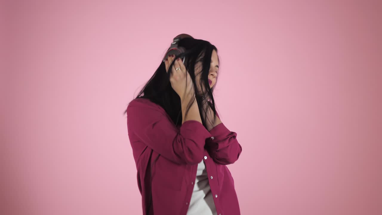 헤드폰을 입은 아름다운 젊은 갈색 여성이 음악을 듣고 컬러 배경에서 노래합니다. 분홍색 셔츠를 입은 행복한 소녀.