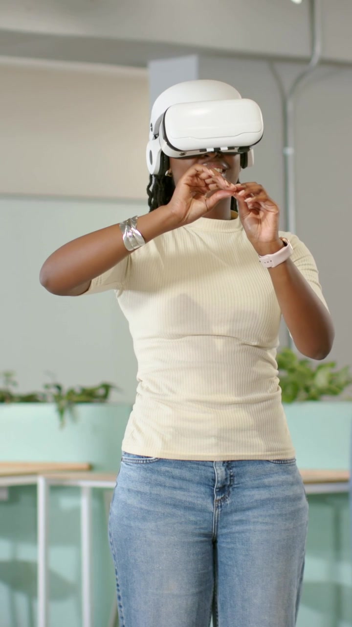 Video verticale: Donna con top beige e jeans che posiziona un visore VR bianco in ufficio, selezionando.