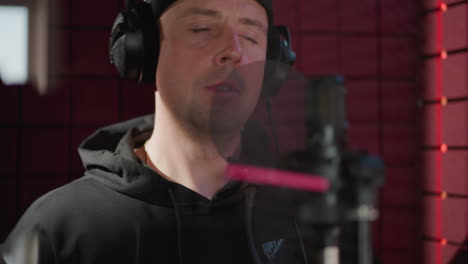 close-up of a man in black standing in front of a microphone in a soundproofed room, putting on studio headphones, as he prepares for a recording session