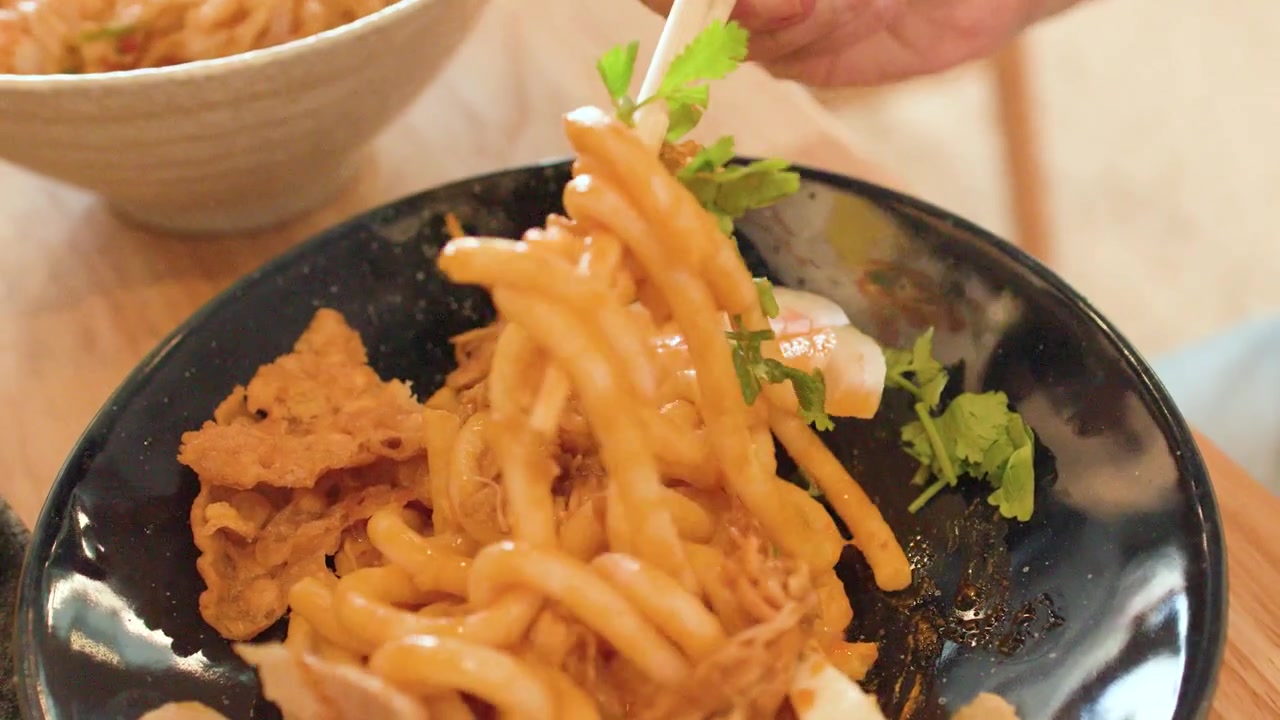 Bacchette mescolano spaghetti di riso spessi con pollo e uovo in una ciotola a Bangkok.