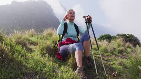 Tired-senior-hiker-woman-sitting-on-grass-while-hiking-in-the-mountains.-trekking