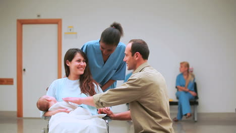 Smiling-nurse-behind-a-mother-and-a-father-with-their-baby-on-a-wheelchair