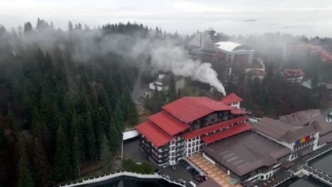 smoke rises from the chimney of a building near the dense forest in poiana brasov, romania