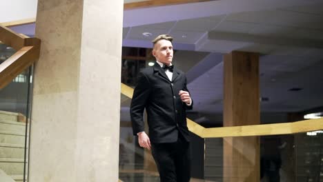 Young-businessman-in-a-suit-with-a-bowtie-is-going-down-the-stairs-in-the-business-center-or-shopping-mall