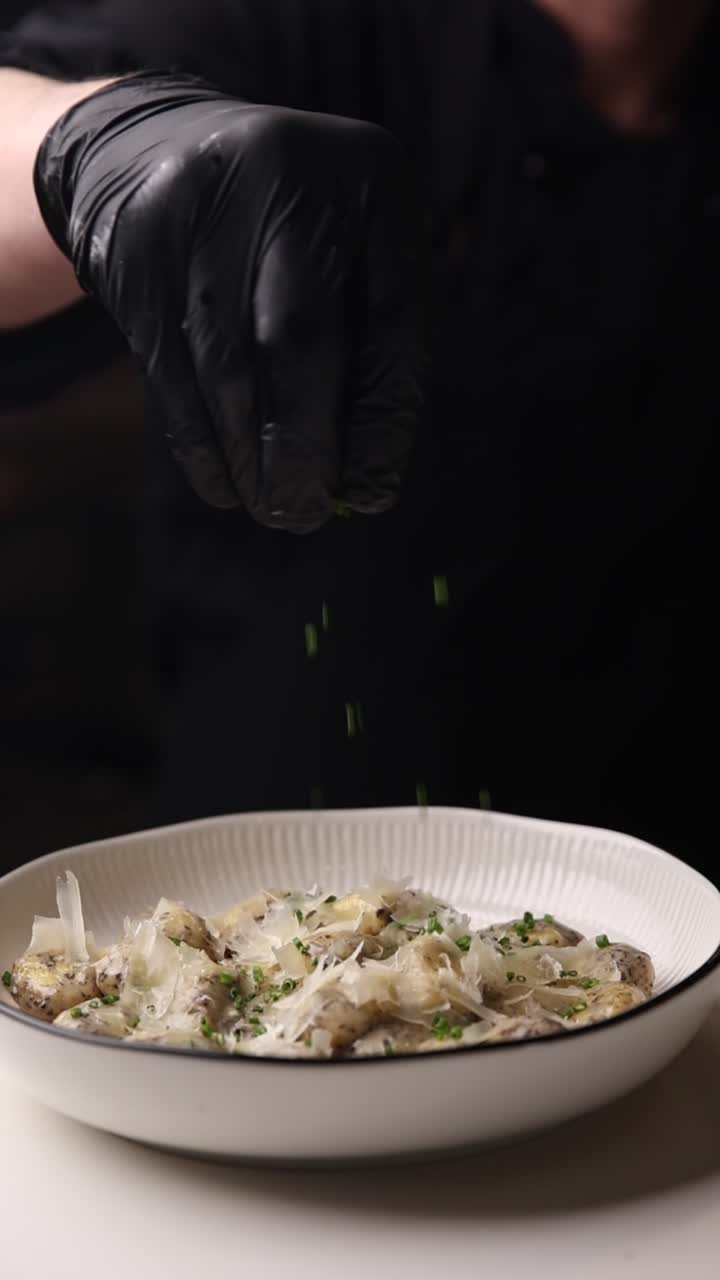 Chef Sprinkling Fresh Chives on Gnocchi with Parmesan Cheese