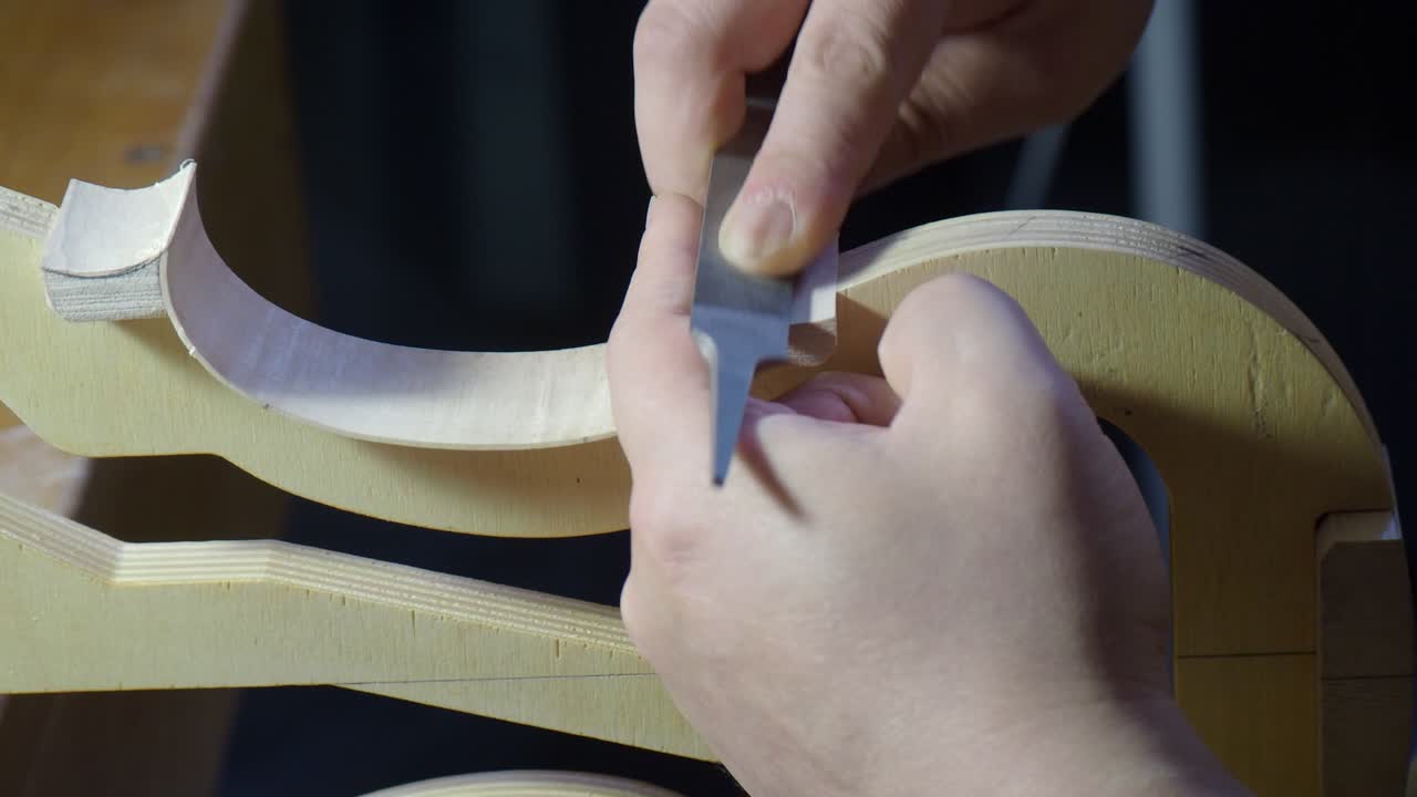 弦楽器職人が内型の上でバイオリンまたはビオラの側板を整形し、楽器製作中に胴体の輪郭と構造を洗練させるため、ブロックの近くで小さな手ヤスリを使って側板のカーブを滑らかにしているクローズアップ