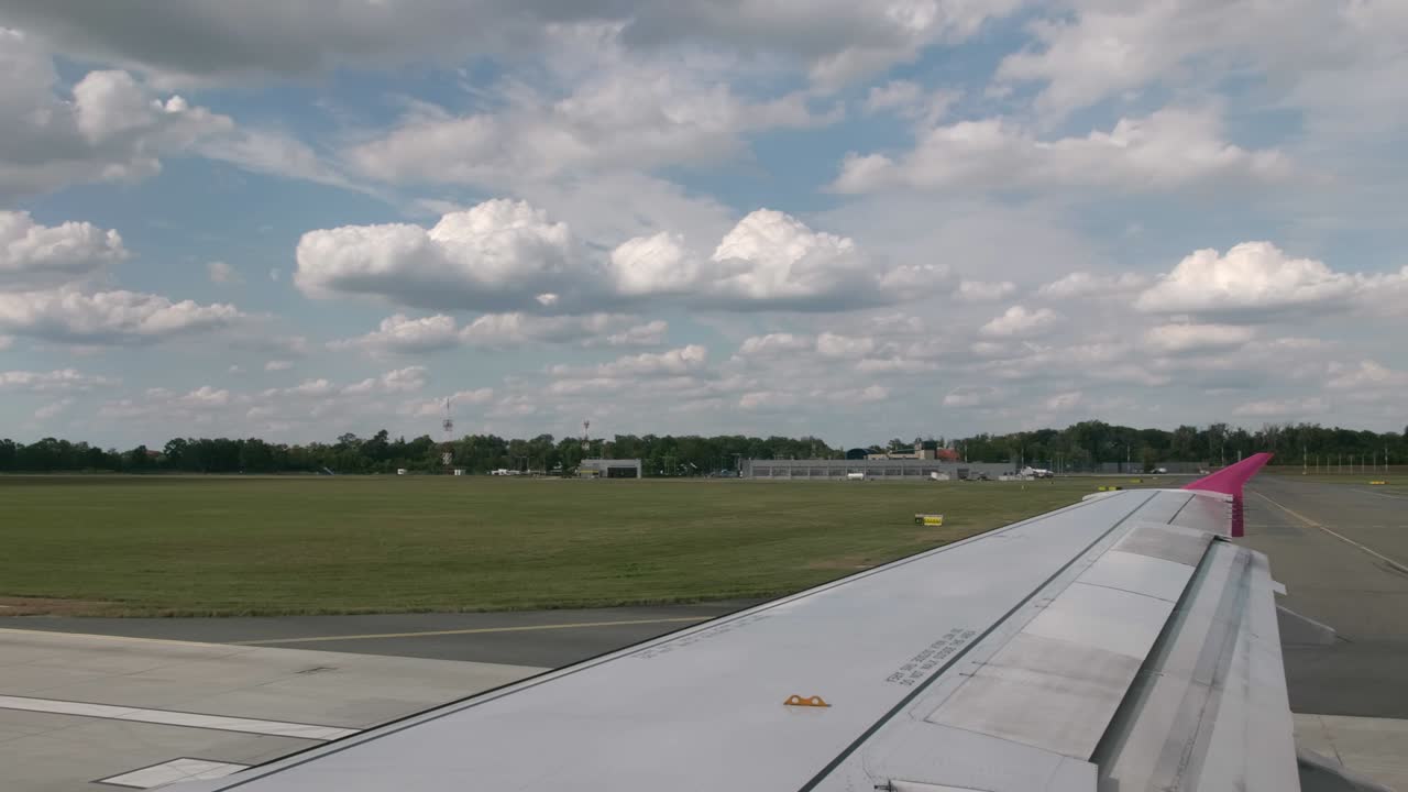 Maneuvering the aircraft at the international airport on the runway. first person view from the cockpit of the aircraft, in the frame a gray wing with a pink wingtip device. In the background is the airport terminal, blue sky and clouds