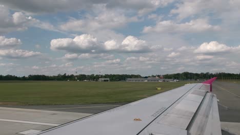 maneuvering the aircraft at the international airport on the runway. first person view from the cockpit of the aircraft, in the frame a gray wing with a pink wingtip device. in the background is the airport terminal, blue sky and clouds