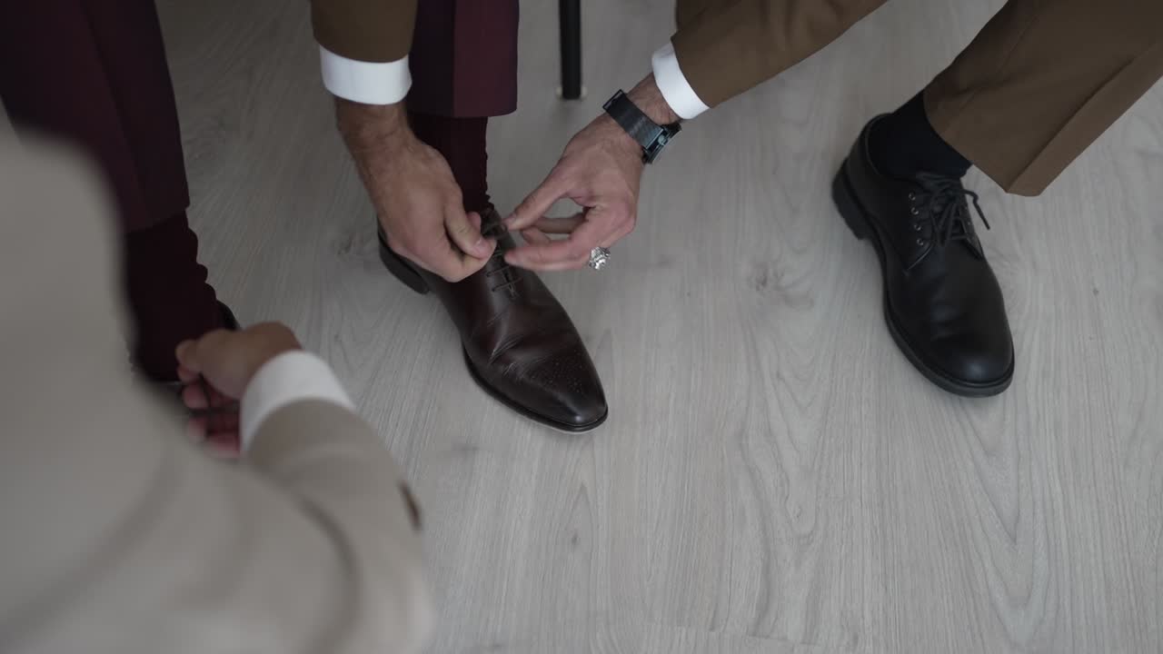 Close up of groom tying brown leather shoe on light wooden floor