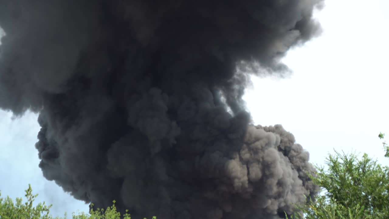 Black smoke rises into the sky. A big chemical fire at a factory building. Thick black smoke covers the sky. 4k