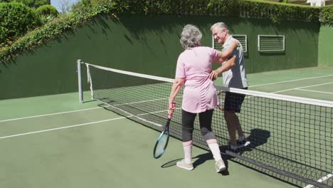 happy caucasian senior couple embracing over the net at outdoor tennis court after playing a game