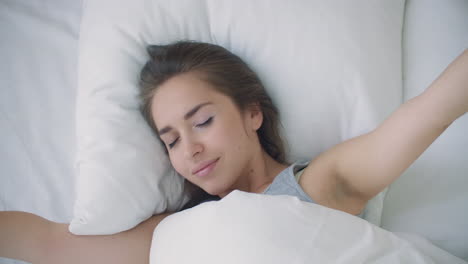 young woman wakes up in bed in the morning smiling raises her hands