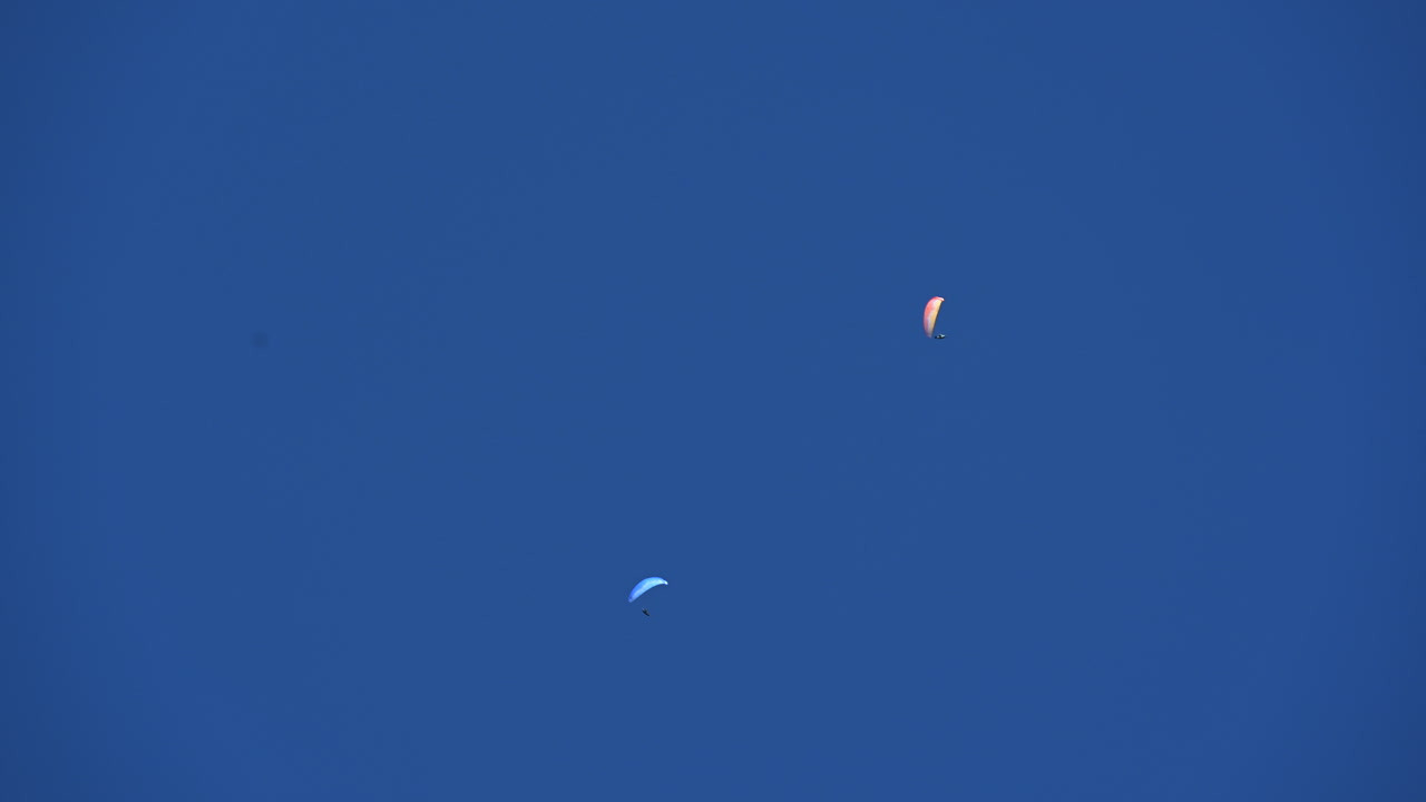 두 개의 낙하산이 스위스 알프스(obwalden) 위의 밝은 푸른 구름 없는 하늘에서 원을 그리며 날아갑니다.