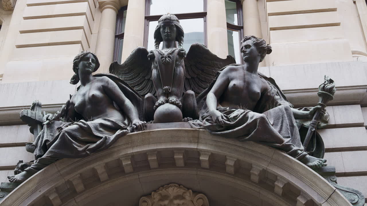 Sculptural group of bronze female and winged figures sitting atop an arched stone building entrance in London, England