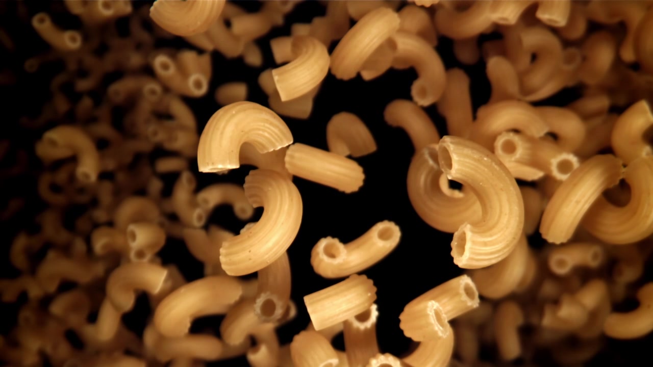 Pasta maccheroni secca che cade al rallentatore su sfondo nero.
