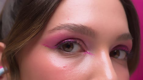 woman with vivid pink makeup looking into the camera under a soft spotlight.