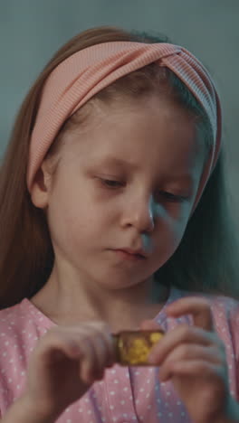 interested little child with pink headband plays with closed small bottle full of white pills in semi-dark room at home extreme close view slow motion