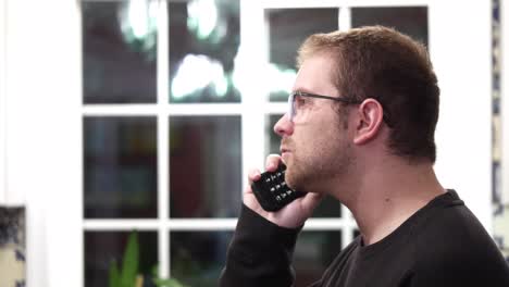 man with glasses makes a call to someone using a retro flip phone, laughs, then hangs up