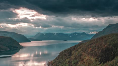 rays of the setting sun shine through stormy clouds over a calm fjord in a time-lapse video