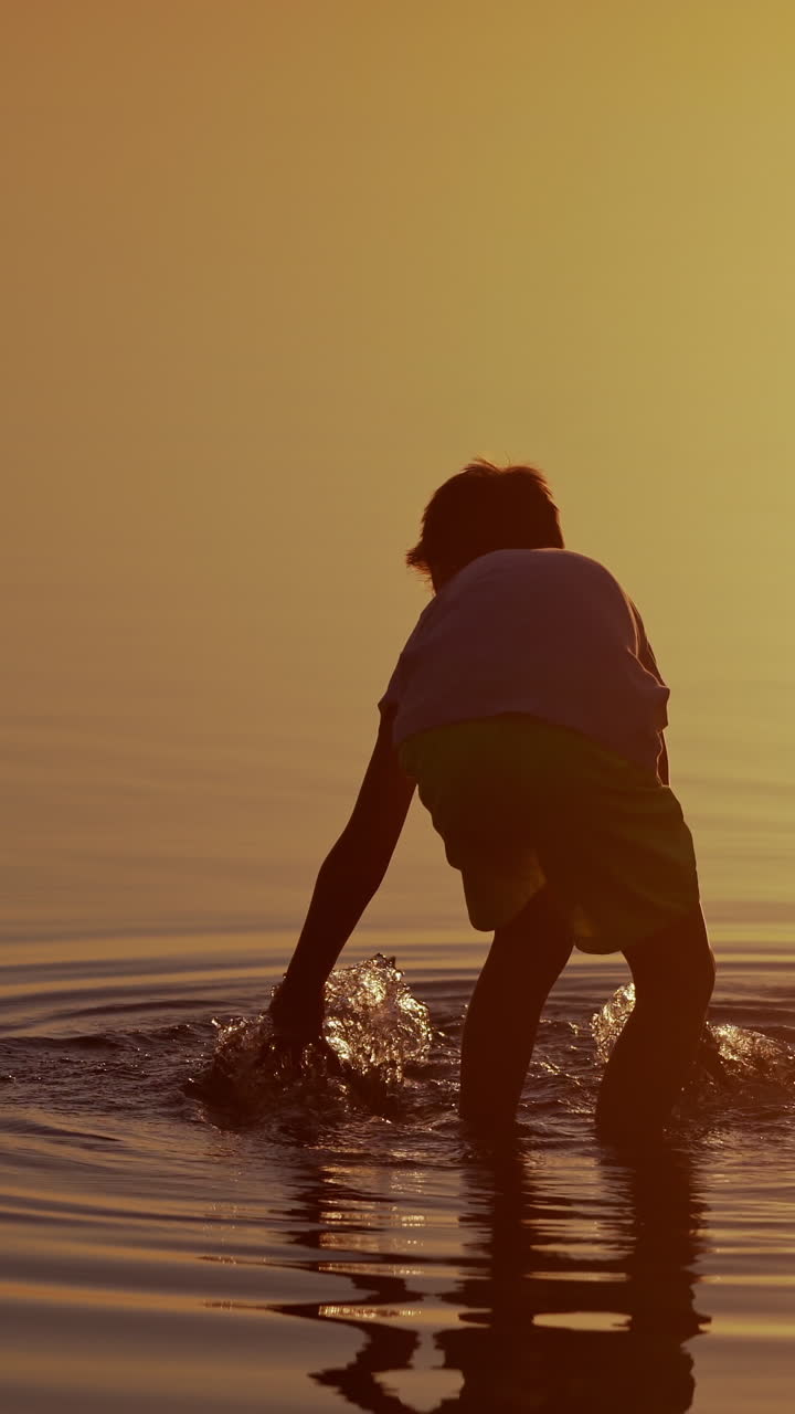 Boy launches Red and green Paper Ships in the river. Origami Paper Boats in kid's hands. Beautiful Waves Ripple Background. Travel and nature Concept. Video at sunset. Vertical video