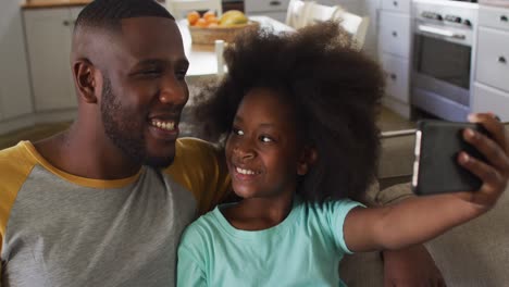 african american daughter and her father taking selfie together sitting on couch smiling