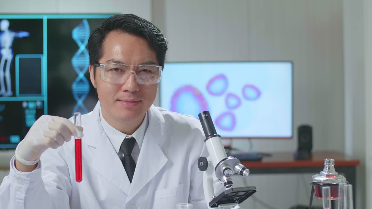 Young Asian Male Research Scientist Looking  Glass Test Tube And Warmly Smiles Into The Camera