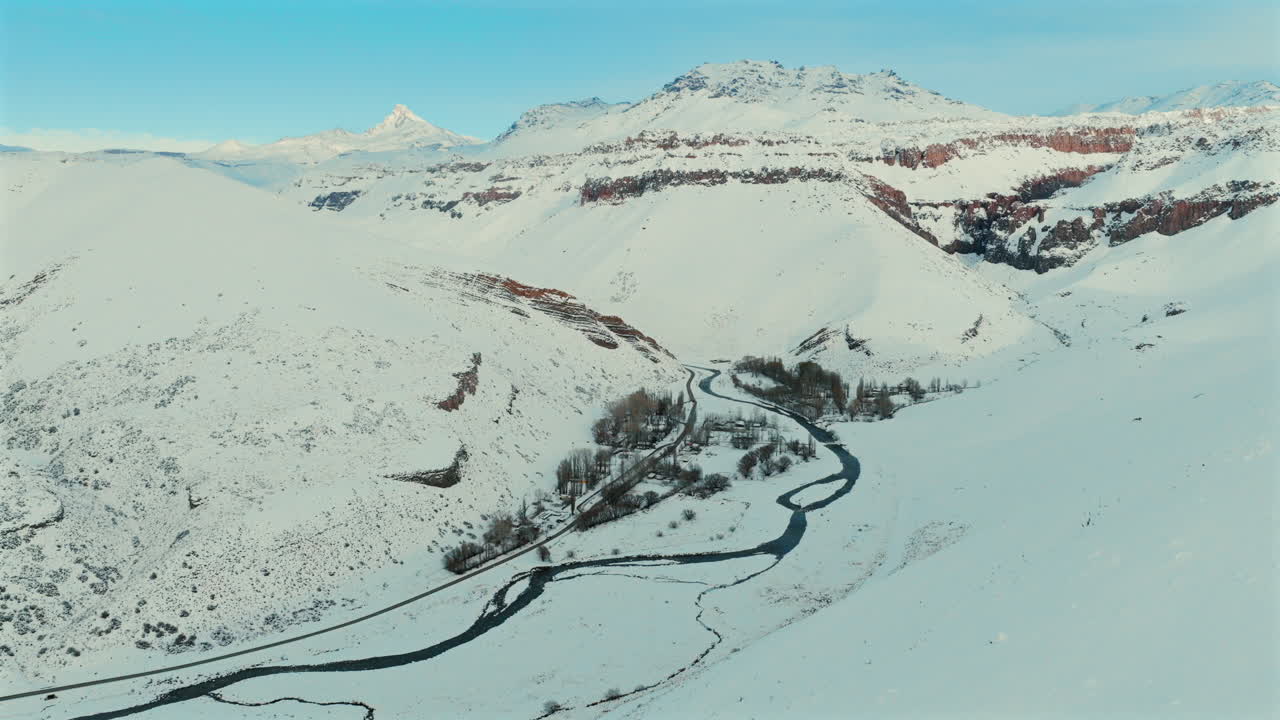 Ascending aerial pullback of snow-capped mountains and winding river in Las Loicas, Paso Pehuenche, Mendoza, during a late winter afternoon