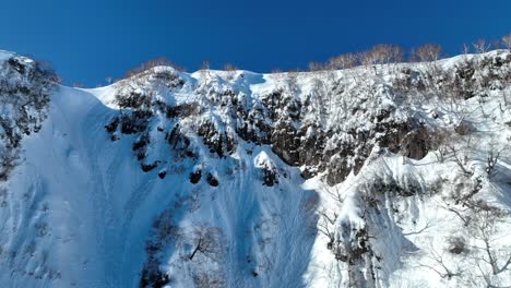 Ascending-shot-flying-up-snow-covered-mountain-cliff-face,-establishing-shot-reveals-mountain-range-and-ocean