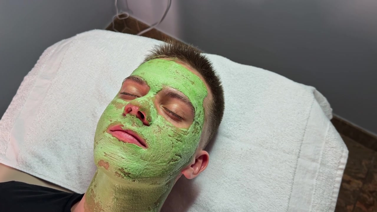 Jovem recebe tratamento facial com máscara verde em um spa durante o dia.