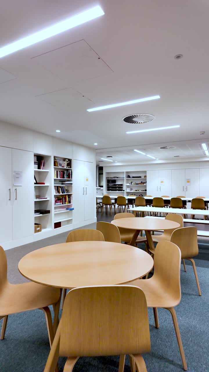 Modern Office Meeting Area With Empty Round Tables And Wooden Chairs White Walls And Shelves Nobody Present For Corporate Or Educational. vertical video