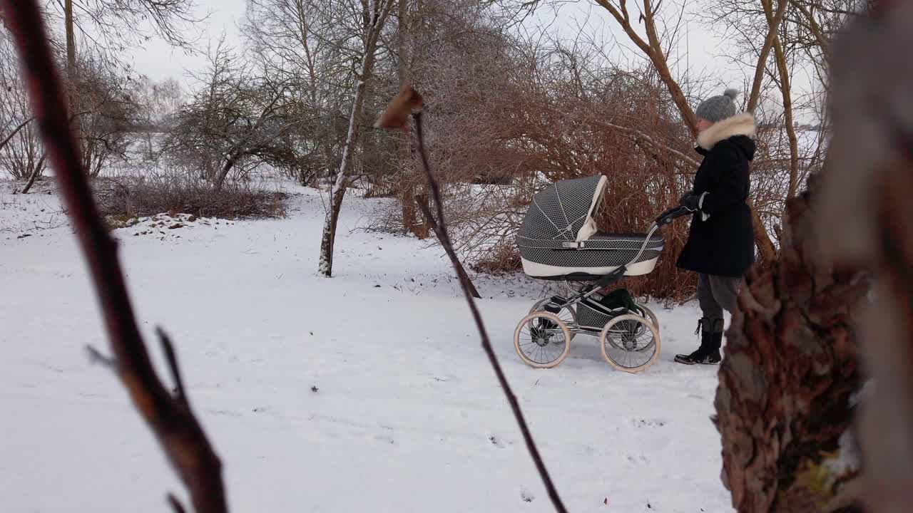En ensamstående mamma går långsamt och skjuter en barnvagn på en snöig landsväg
