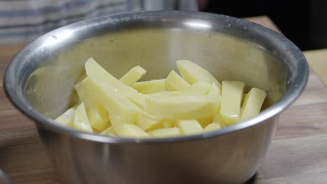 a chef pours olive oil over raw potato wedges in a metal bowl