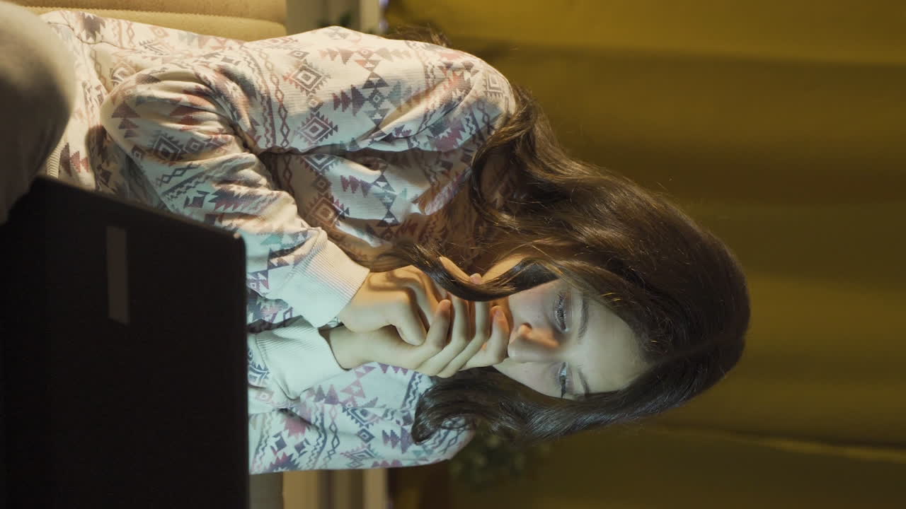 밤에 노트북에서 공포 영화를 보는 젊은 여성의 수직 비디오.